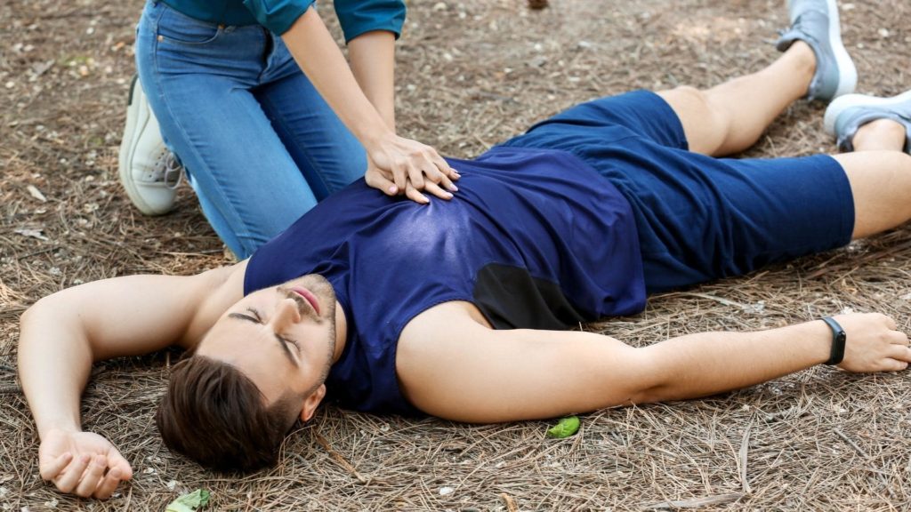 Person performing CPR on a man lying on the ground, representing emergency response to a heart attack.