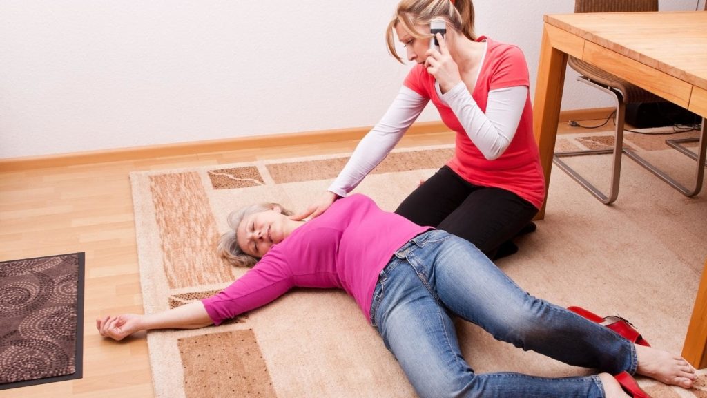 Person on the phone checking the pulse of a woman lying on the ground