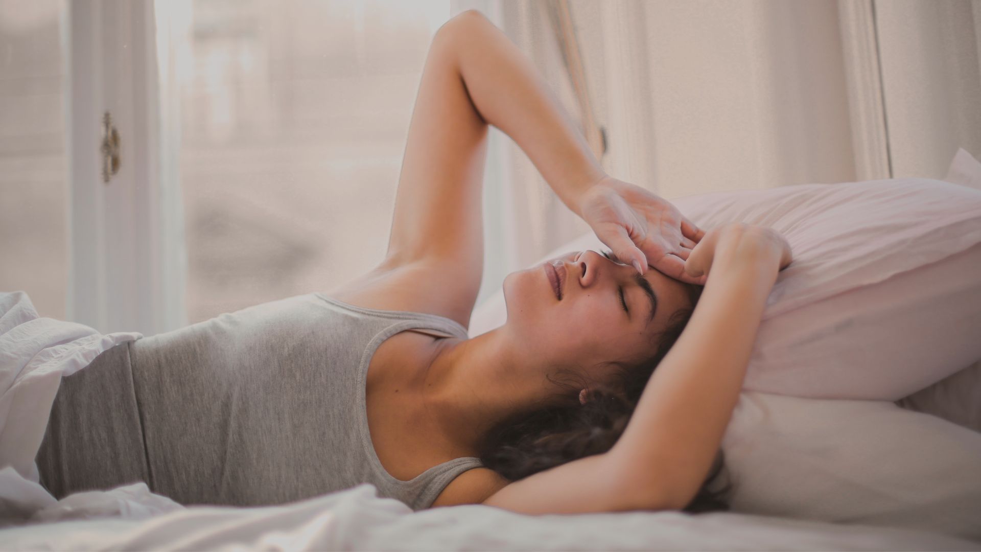 Woman laying in bed, with what seems a headache