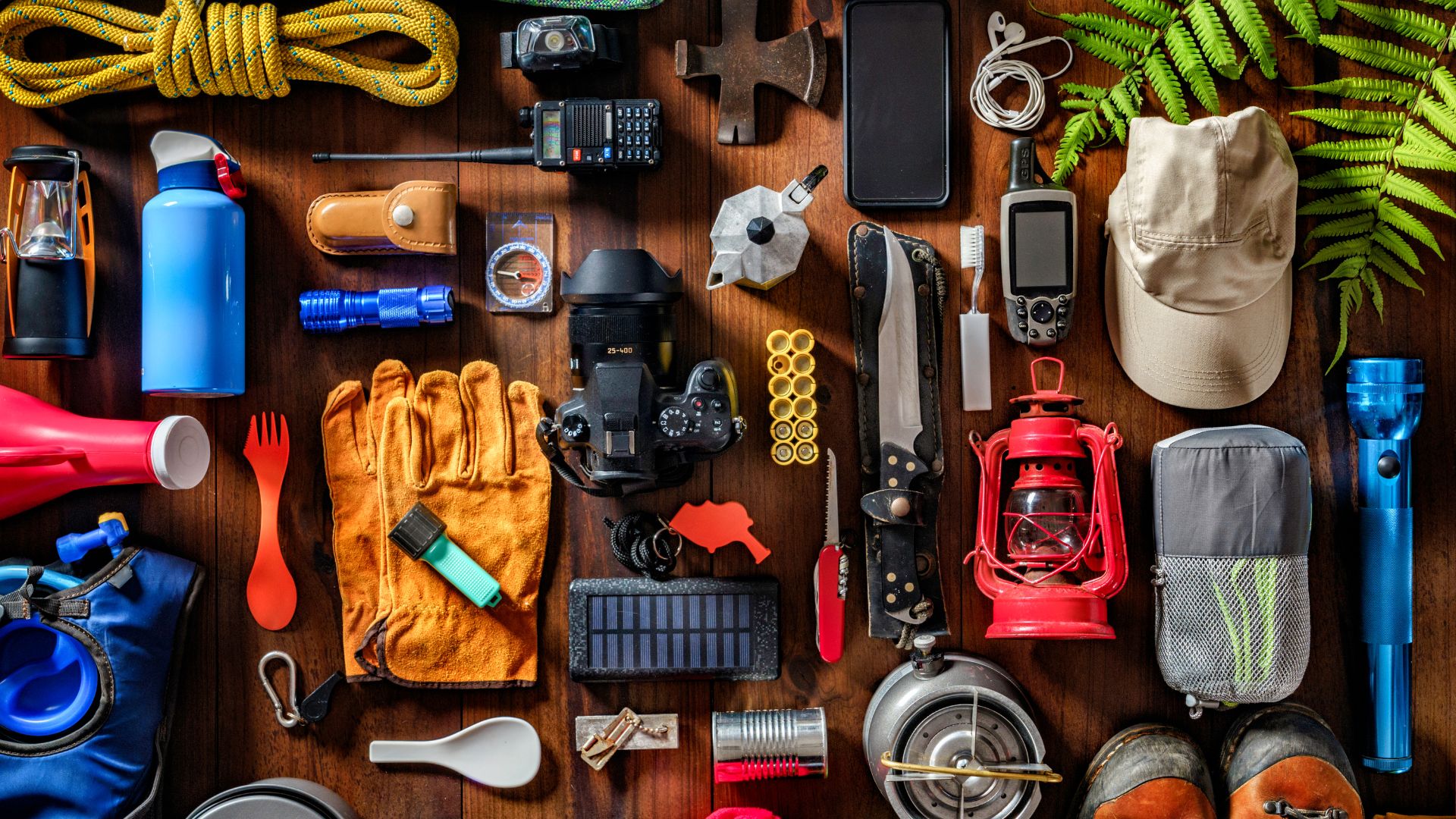 A variety of hiking gear, including backpacks, knives, water bottles, and boots, laid out for preparation