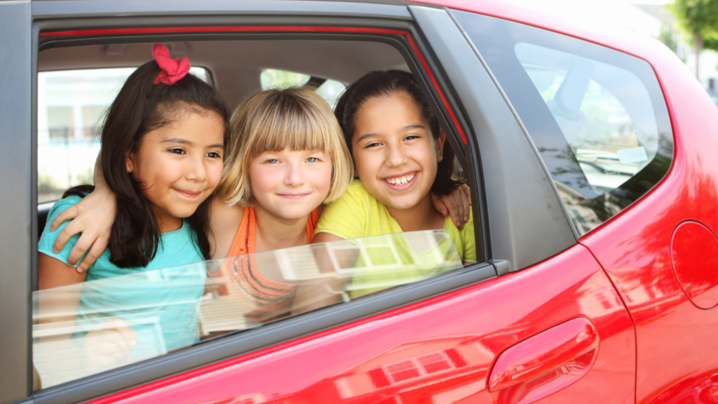 Three kids staring out of the window of a red car while car pooling