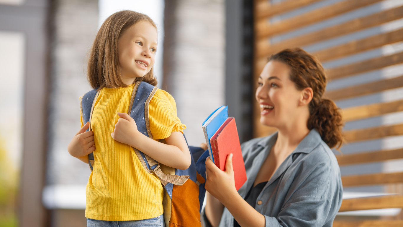 A child wearing a backpack and a mother bending to put books in the backpack.