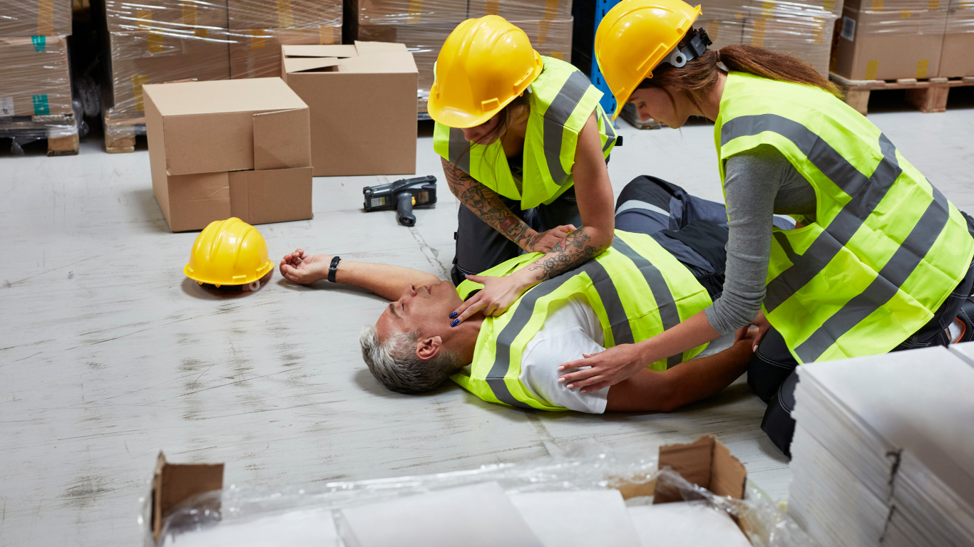 Two construction workers providing first aid to an injured colleague on a construction site, demonstrating the importance of safety training