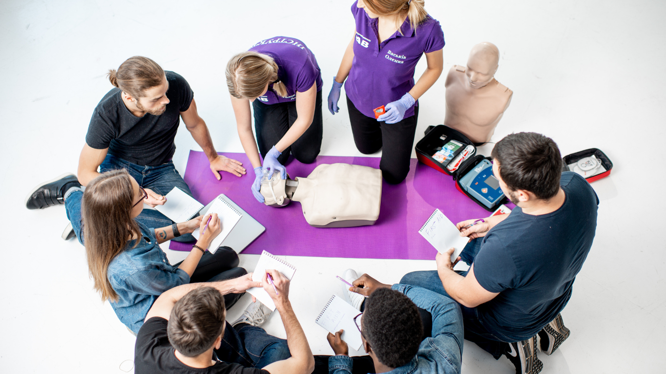 A group of people surrounding an instructor performing CPR training on a mannequin 