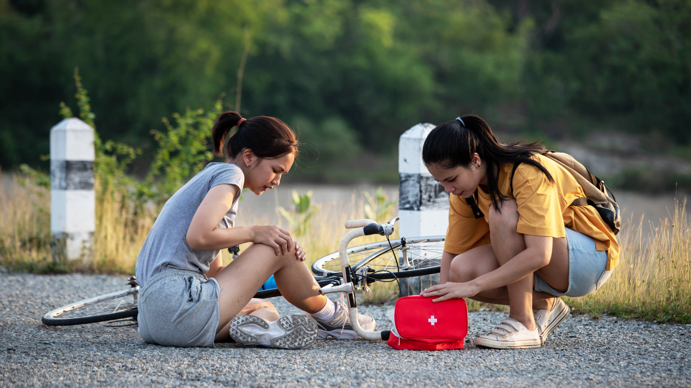 A girl administering first aid on another girl after falling off a bicycle.