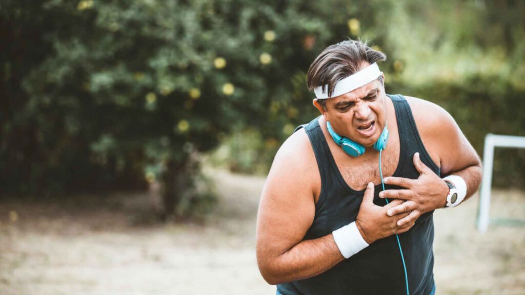 A man exercising outside with his hand oh his chest responding to pain.